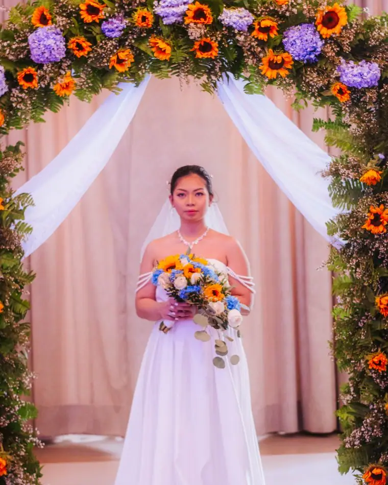 A bride standing beneath a sunlit floral arch